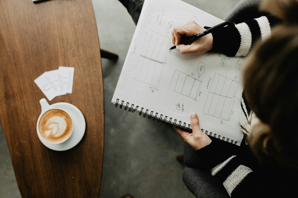 Mulher traçando metas financeiras em um caderno, com uma xícara de café ao lado, representando foco e organização pessoal.