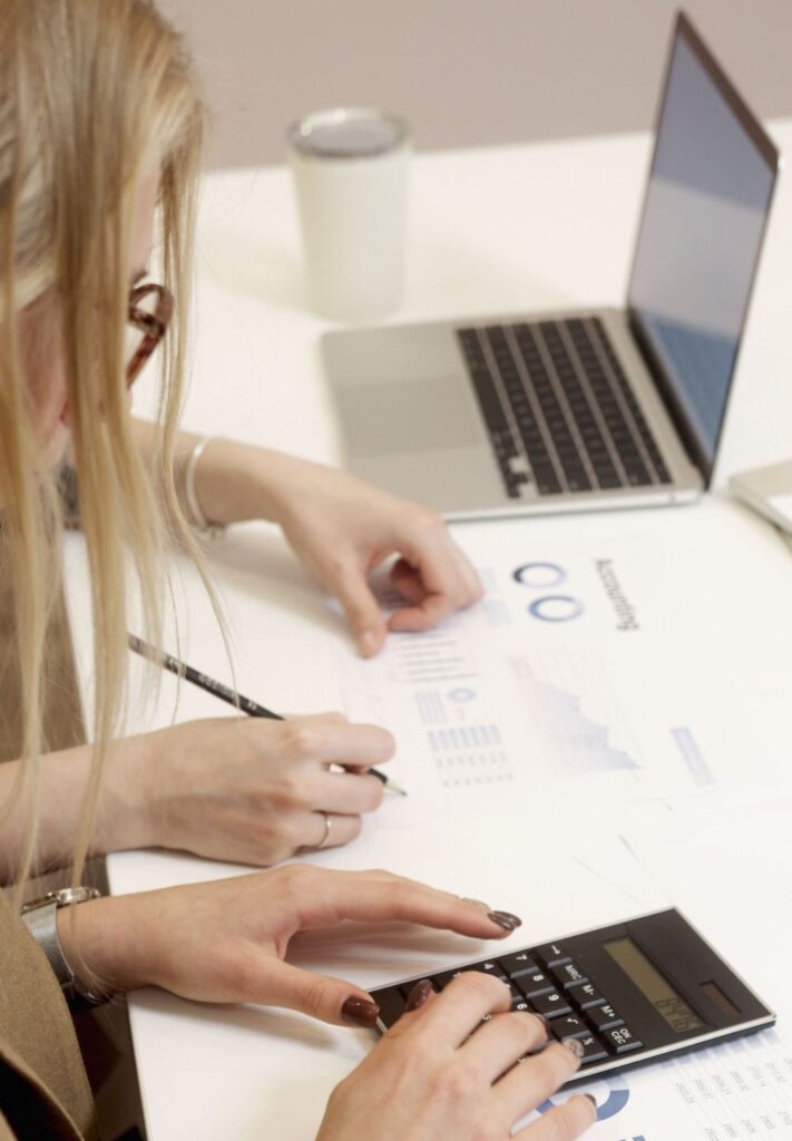 Mulher analisando gráficos financeiros e utilizando uma calculadora para comparar investimentos em renda fixa e renda variável.