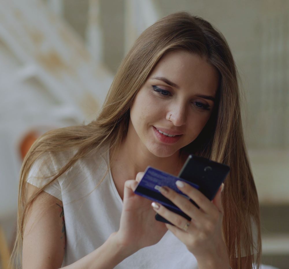 Mulher realizando uma compra online pelo celular e cartão de crédito para receber cashback.