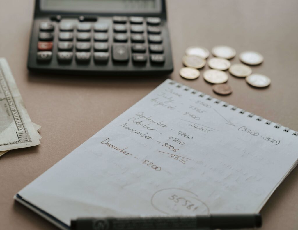 Pessoa organizando o orçamento financeiro com calculadora, anotações, moedas e dinheiro sobre a mesa.