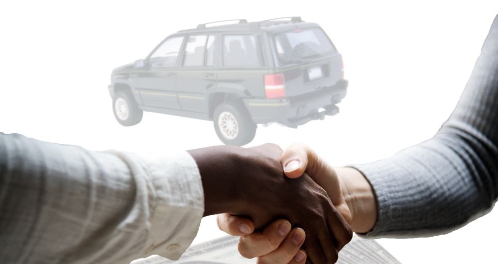 Duas pessoas apertando as mãos durante uma negociação, com a imagem de um carro ao fundo, representando um acordo para a compra de um veículo por meio de planejamento financeiro.