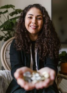 Mulher sorrindo enquanto segura moedas nas mãos, representando o hábito de economizar e a construção de uma reserva financeira.