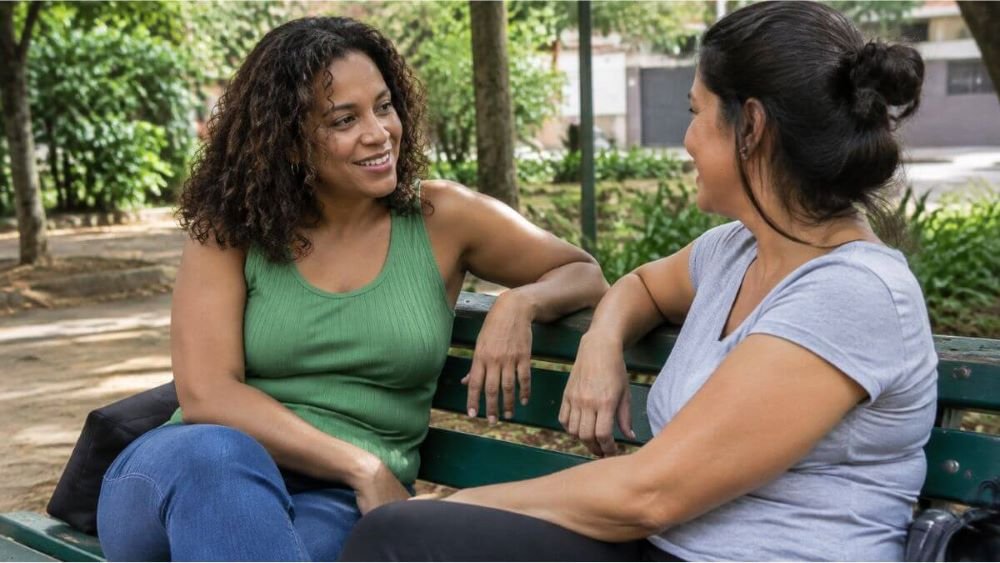 Duas mulheres conversam em um banco de praça durante um momento de lazer.